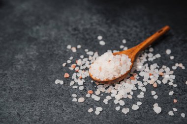 Ahşap kaşık pembe himalaya tuzu ve dokulu siyah yüzey.