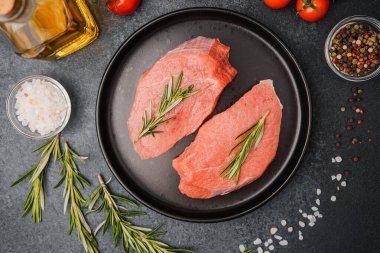 Siyah seramik tabakta çiğ biftek, biberiye, kiraz, domates, tuz ve biber.