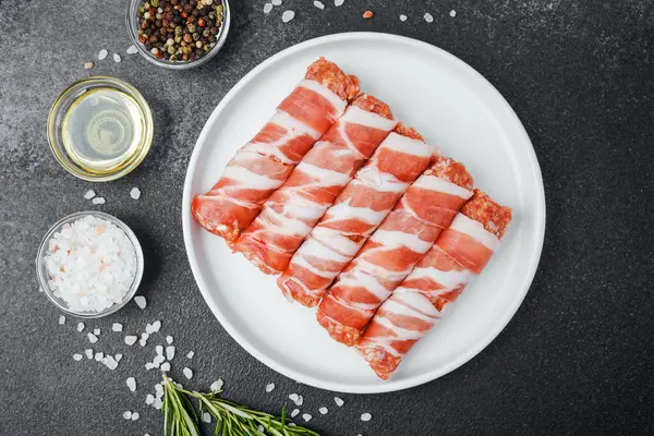 Çiğ domuz pastırması beyaz tabağa sarılmış, baharatlı ve otlu.