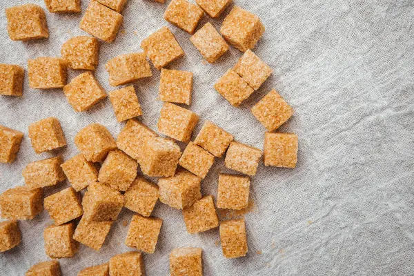 Kahverengi şeker küpleri mutfaktaki dokulu keten kumaşa saçılmıştır..