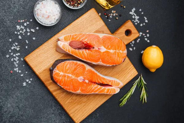 Tahtaya dizilmiş somon filetoları. Yanında otlar, limon ve baharatlar var..