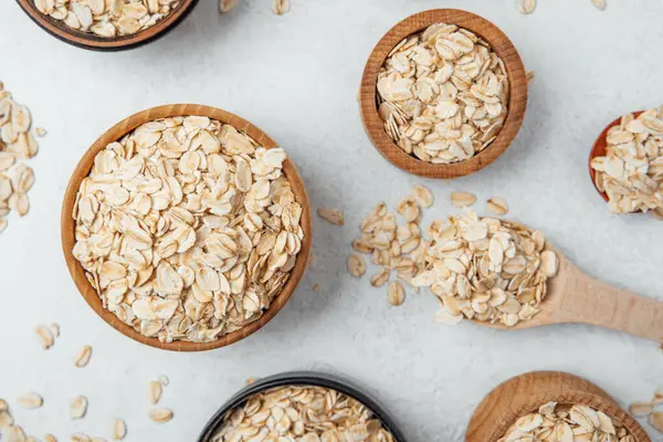 Yulaf dolu çeşitli kaseler gevşek taneli hafif bir yüzeyde sergilenir..