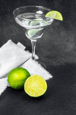 Kristal bir cam, koyu bir yüzeyde taze limonların yanında limonlu bir içecek tutar..