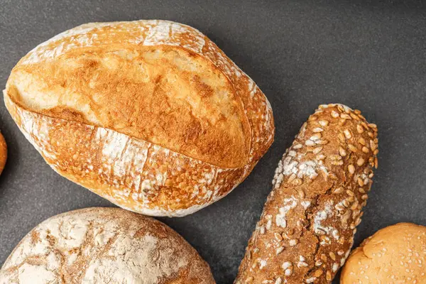 Koyu bir tezgahta çeşitli ekmekler sergileniyor, dokuları vurgulanıyor..