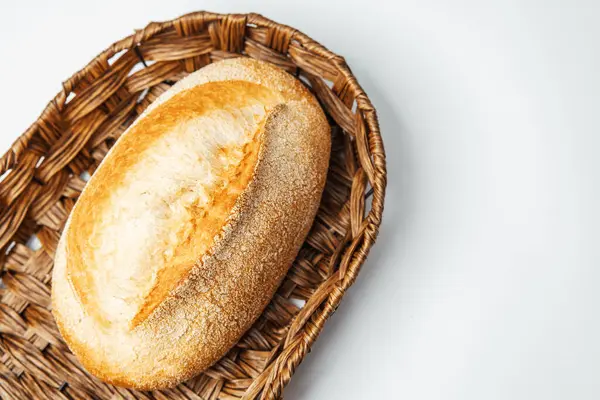 Bir somun kabuklu ekmek sade bir arka planda sade bir hasır sepette duruyor..