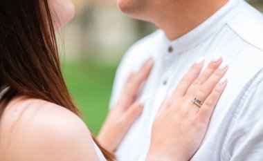 Bir çift açık havada hassas bir anın tadını çıkarıyor, yakın odak noktasında nişan yüzüğü sergiliyor..