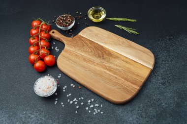 Kiraz domatesli tahta kesmek otlar, tuz ve baharatlar koyu arka planda.