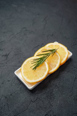 Koyu taş zemin üzerinde küçük beyaz tabakta biberiyeli limon dilimleri.