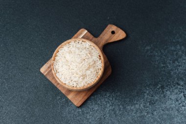 Beyaz basmati pilavı ahşap kase içinde kesme tahtasının üzerinde koyu arkaplanda