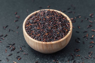 Tahta kasede saçılmış tanelerle çevrili siyah pirinç.