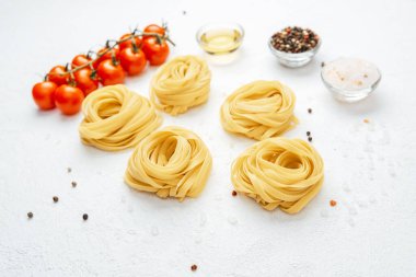 Beyaz arka planda domates ve baharatlı çiğ tagliatelle makarnası.