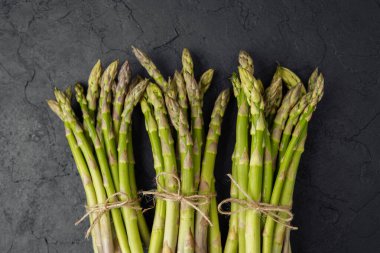 Siyah arka planda sicimle bağlanmış üç demet yeşil kuşkonmaz