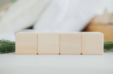 Üniformalı üç ahşap blok, yeşilliklerle çevrili açık renkli bir masanın üzerine güzelce yerleştirilir. Ayar parlak ve minimalistik, doğal ahşap tonlarını güçlendiriyor..