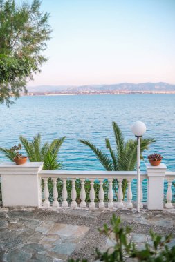 Yunanistan 'da Pastel gökyüzü altında palmiye ağaçları ve deniz manzaralı kıyı verandası