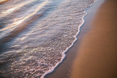Gün batımında kumlu sahilde hafif okyanus dalgaları.