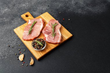 İki domuz pirzolası, biberiye ve baharatla süslenmiş bir kesme tahtasının üzerinde oturur..