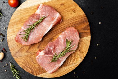 Tahtaya yerleştirilmiş taze domuz eti ve etrafa saçılmış biberiye ve baharatlar..