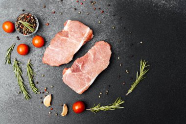 Domates, sarımsak ve bitkilerle hazırlanmış iki parça çiğ domuz pirzolası..