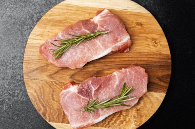 Ağaç kesme tahtasına biberiyeyle süslenmiş iki çiğ domuz pirzolası..