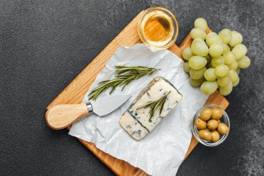 Bir gurme peynir tahtasında mavi peynir, üzüm, zeytin ve bir bardak şarap bulunur..