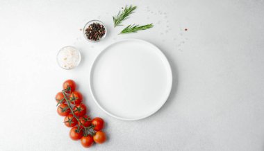 Beyaz arka planda tuz, biber, domates ve biberiye ile boş beyaz tabak