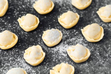 Siyah taş zemin üzerine un serpiştirilmiş taze pişmemiş cappelletti.