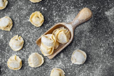 Ahşap kepçeyle un kaplı koyu arkaplanda çiğ kapel makarna.