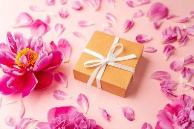 Beyaz kurdeleli hediye kutusu ve pastel arka planda pembe şakayık çiçekleri dağınık taç yapraklarıyla