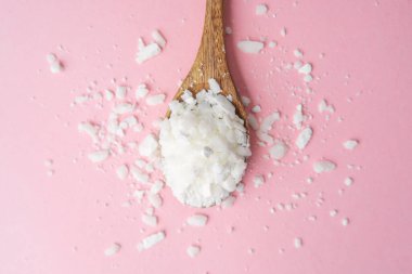 Ahşap kaşık, temiz pembe arka planda soya yağı tanecikleri.