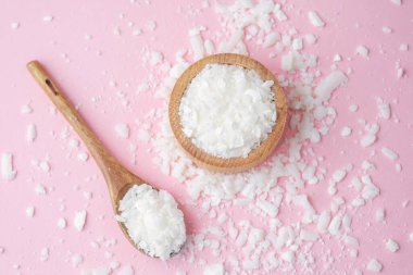 Ahşap kase ve kaşık, pastel pembe arka planda soya yağı taneleri.