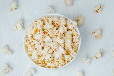 A bowl filled with fluffy popcorn sits among scattered kernels, inviting snack lovers.
