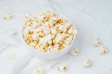 Kabarık patlamış mısırla dolu bir kase, etrafa saçılmış parçalarla beyaz bir kumaşın üzerinde duruyor..