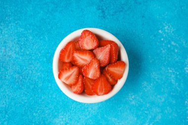 Mavi arka planda bir kase taze dilimlenmiş çilek.