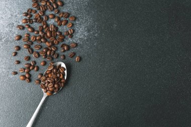 Koyu arkaplanda metal kaşıkta kahve çekirdekleri