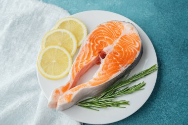 Limon dilimli çiğ somon bifteği ve mavi arka planda beyaz tabakta biberiye.