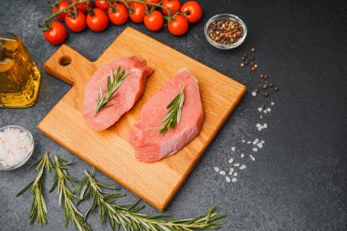 Kesme tahtasında biberiyeli çiğ biftek. Etrafı kiraz domatesleri, yağ tuzu ve biberle çevrili.