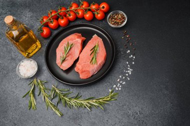 Siyah seramik tabakta çiğ biftek, biberiye, kiraz, domates, tuz ve biber.