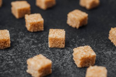 Küçük kahverengi şeker küpleri koyu bir tezgah yüzeyinde gelişigüzel düzenlenir..