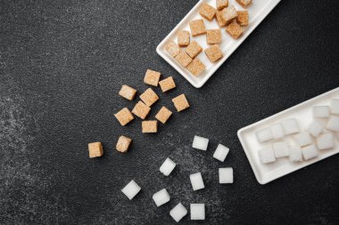 Kahverengi ve beyaz şeker küpleri siyah mermer üzerinde ayrı tepsilerde sergilenir..