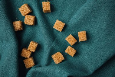 Kahverengi şeker küpleri, gümüş bir kumaş üzerinde gelişigüzel düzenlenir ve sıcak bir kontrast oluşturur..