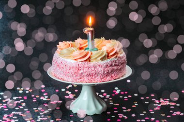 Güzel dekore edilmiş, kremalı pembe bir pasta ve doğum gününü kutlayan bir mum..