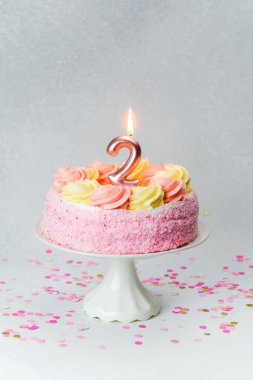 Çiçek şekerli pembe bir pasta, etrafında köpüklü konfeti olan bir tezgahta oturur..