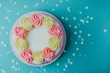 Süslü, pembe ve sarı kremalı bir pasta konfetili bir deniz mavisi yüzeyinde oturur..