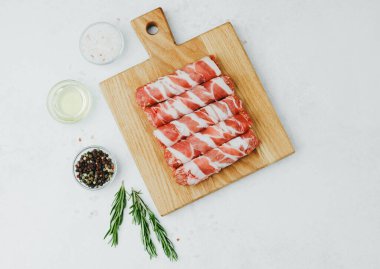 Domuz pastırmasına sarılı sosisli börekler, ahşap tahtada otlarla.