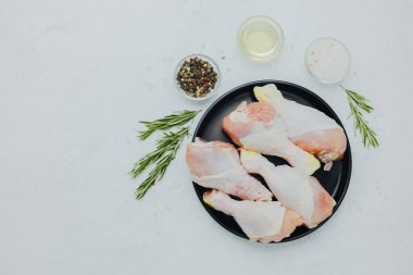 Biberiye ve baharatlı siyah tabakta çiğ tavuk budu.