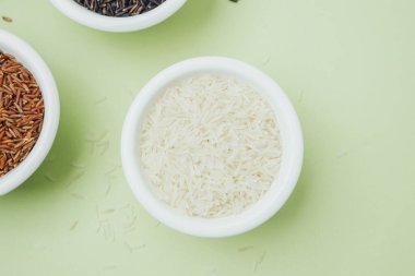 Top view of black red and white rice in ceramic bowls on green background