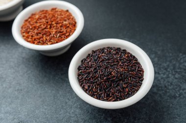 Koyu arkaplan manzaralı kaselerde üç çeşit pirinç.