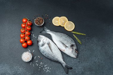 Domatesli taze çiğ dorado balığı limon ve siyah arka planda baharatlar.
