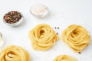 Beyaz arka planda domates ve baharatlı çiğ tagliatelle makarnası.