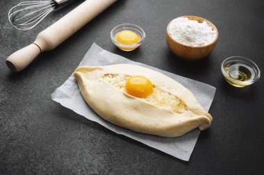 Parşömen üzerinde peynir ve sarısı olan Khachapuri ve koyu mutfak masası.